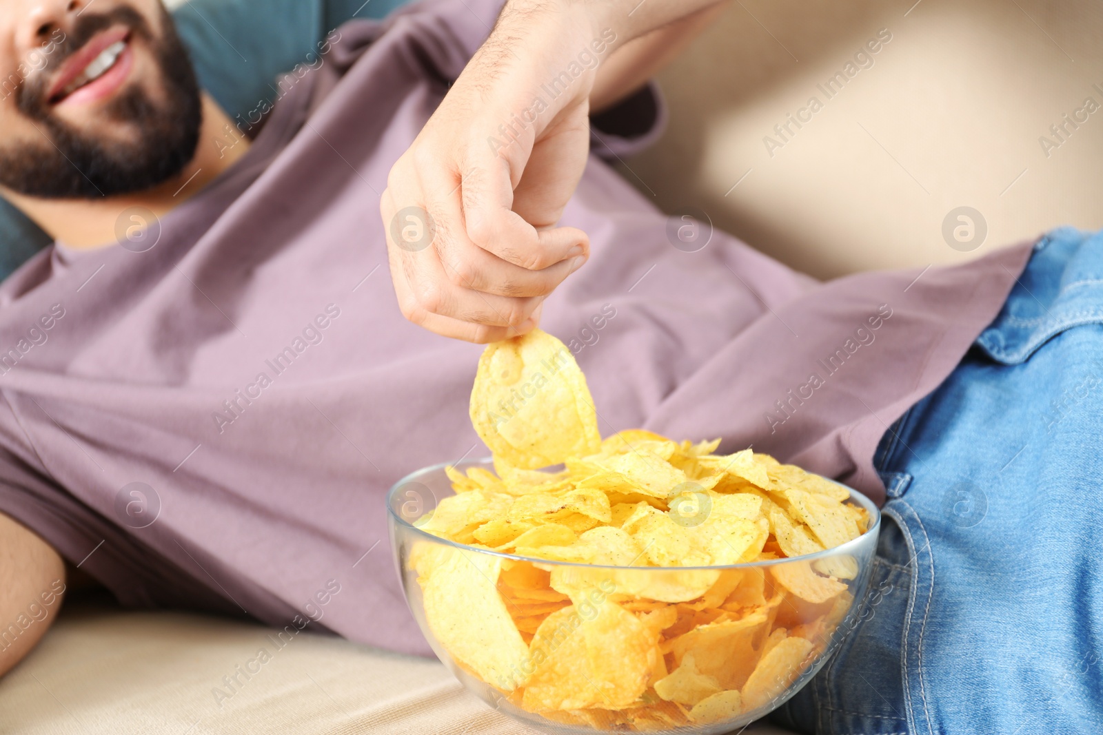 Photo of Man eating chips while watching TV on sofa, closeup