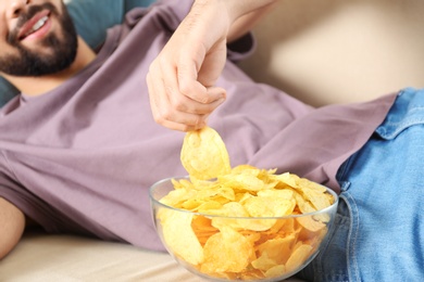 Photo of Man eating chips while watching TV on sofa, closeup
