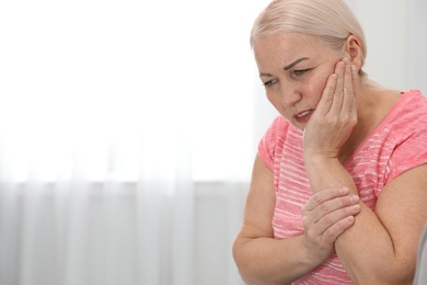 Photo of Mature woman suffering from strong tooth pain at home, space for text