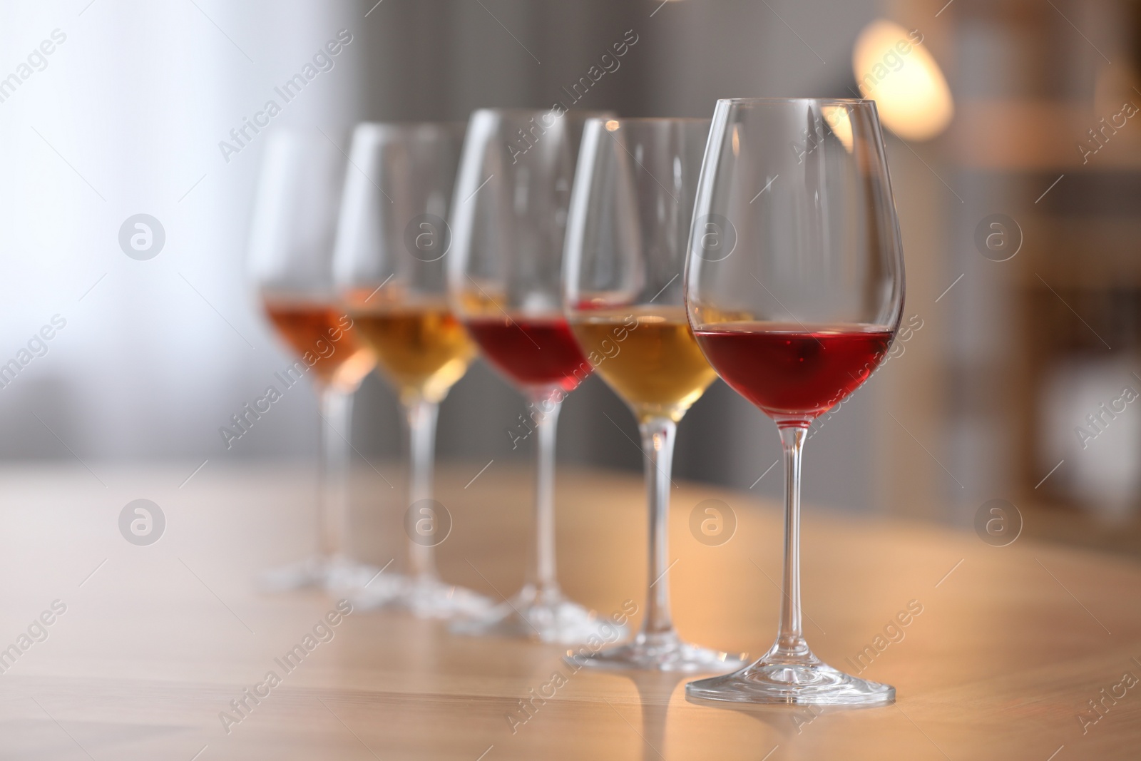 Photo of Different sorts of wine in glasses prepared for tasting on wooden table indoors