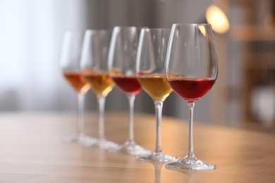 Photo of Different sorts of wine in glasses prepared for tasting on wooden table indoors