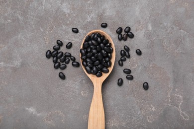 Photo of Spoon of raw black beans on grey table, top view