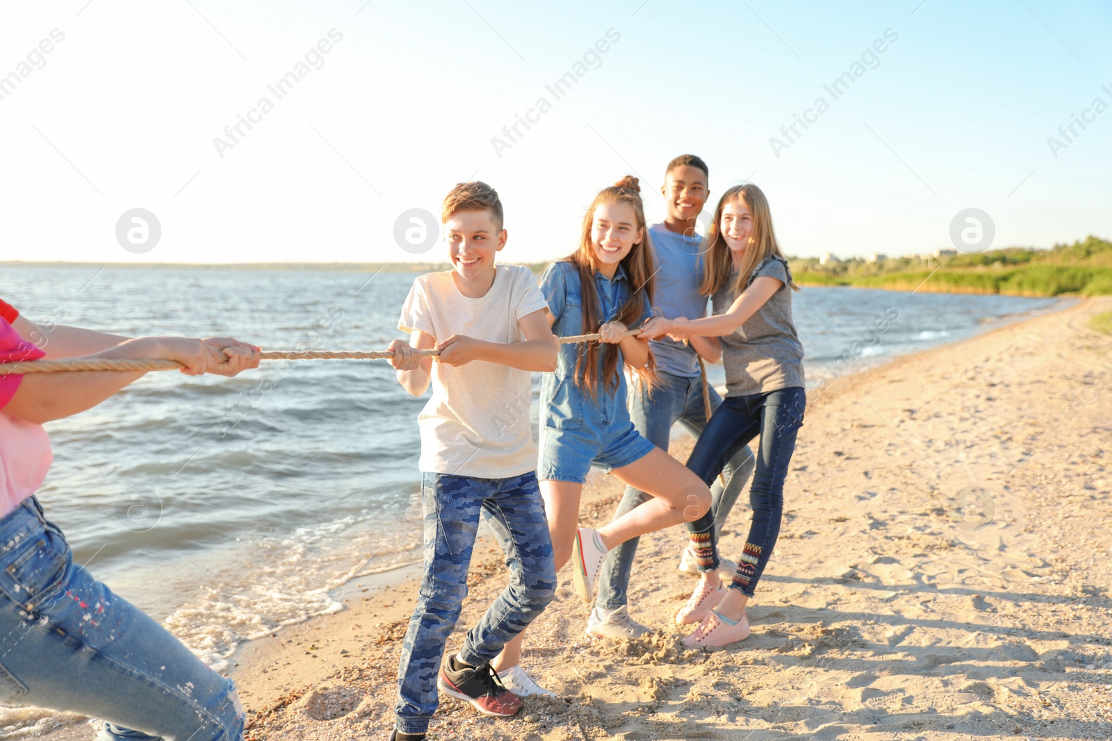 Photo of Group of children pulling rope during tug of war game on beach. Summer camp