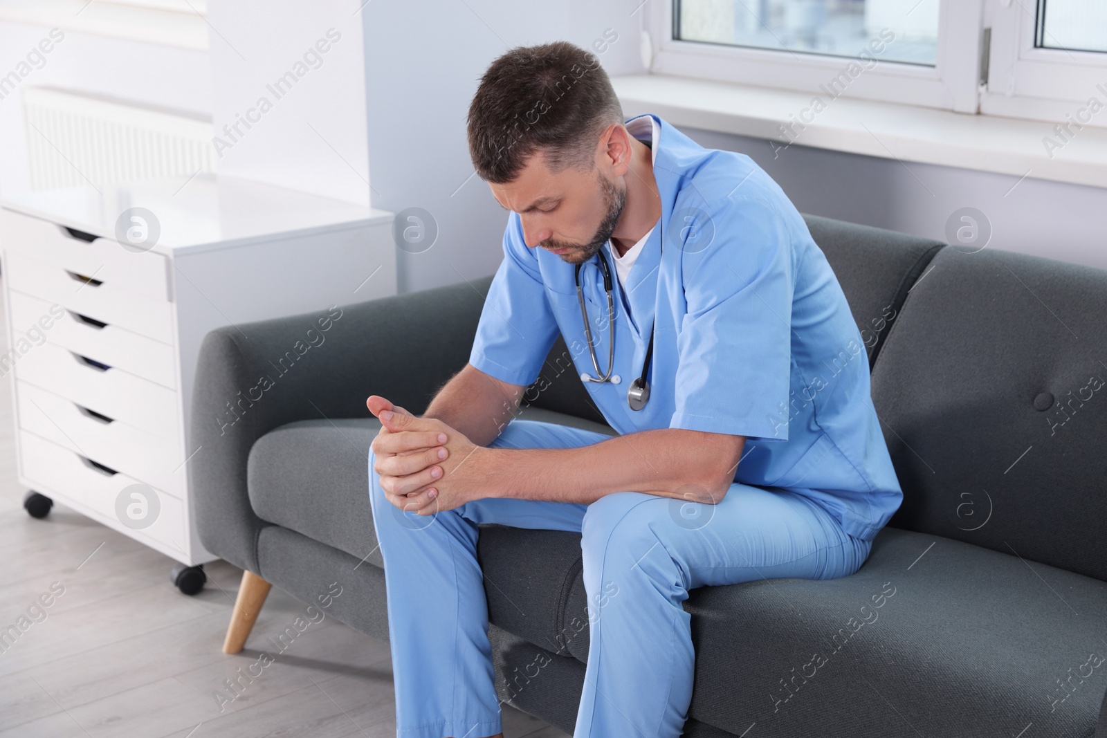 Photo of Exhausted doctor sitting on sofa in hospital