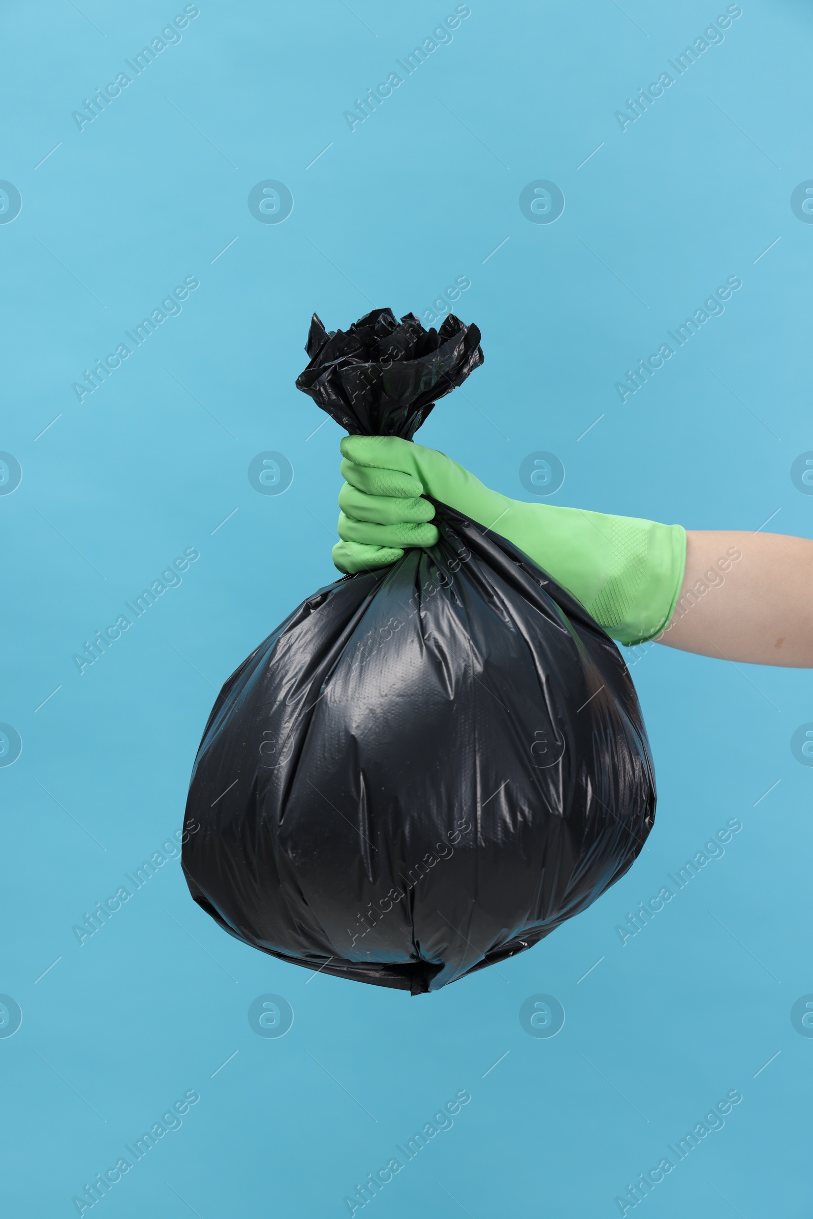 Photo of Woman holding plastic bag full of garbage on light blue background, closeup