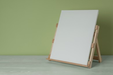 Photo of Wooden easel with blank canvas on white table. Space for text