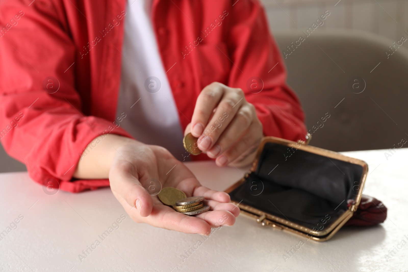 Photo of Poor woman counting coins at white table indoors, closeup
