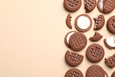 Tasty chocolate sandwich cookies with cream on beige background, flat lay. Space for text