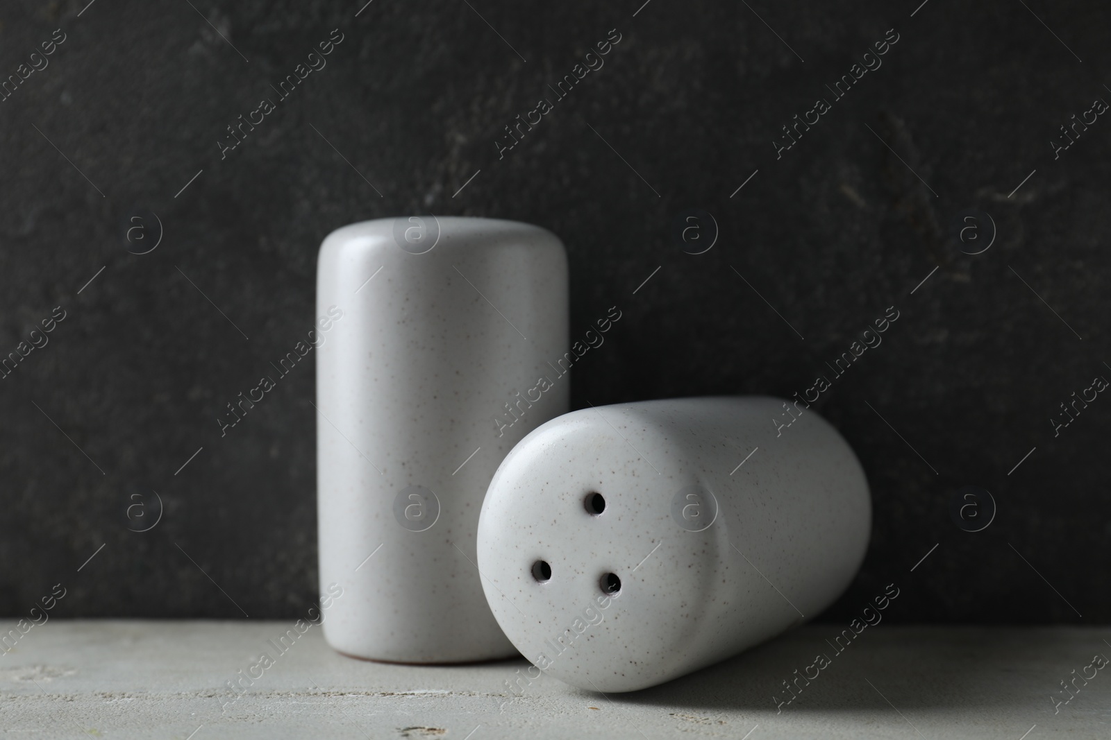 Photo of Salt and pepper shakers on light table against grey background, closeup