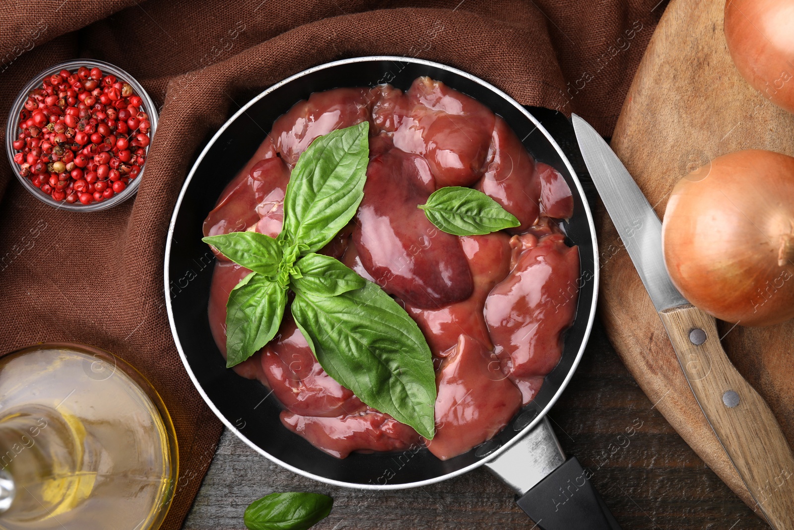 Photo of Raw chicken liver with basil in frying pan and products on wooden table, flat lay