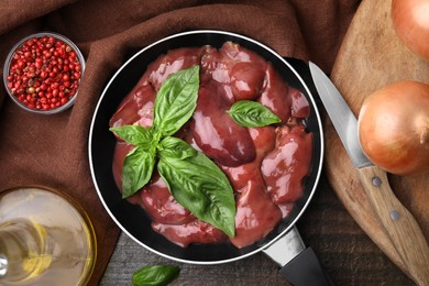 Raw chicken liver with basil in frying pan and products on wooden table, flat lay