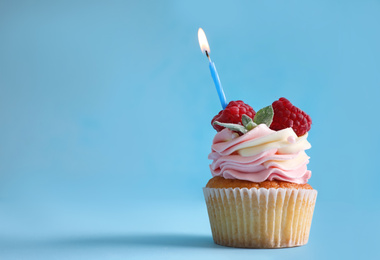 Photo of Delicious birthday cupcake with raspberries and burning candle on light blue background. Space for text