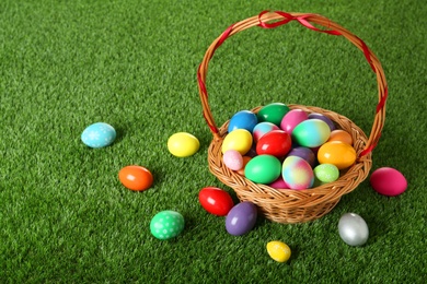 Photo of Wicker basket with Easter eggs on green grass.