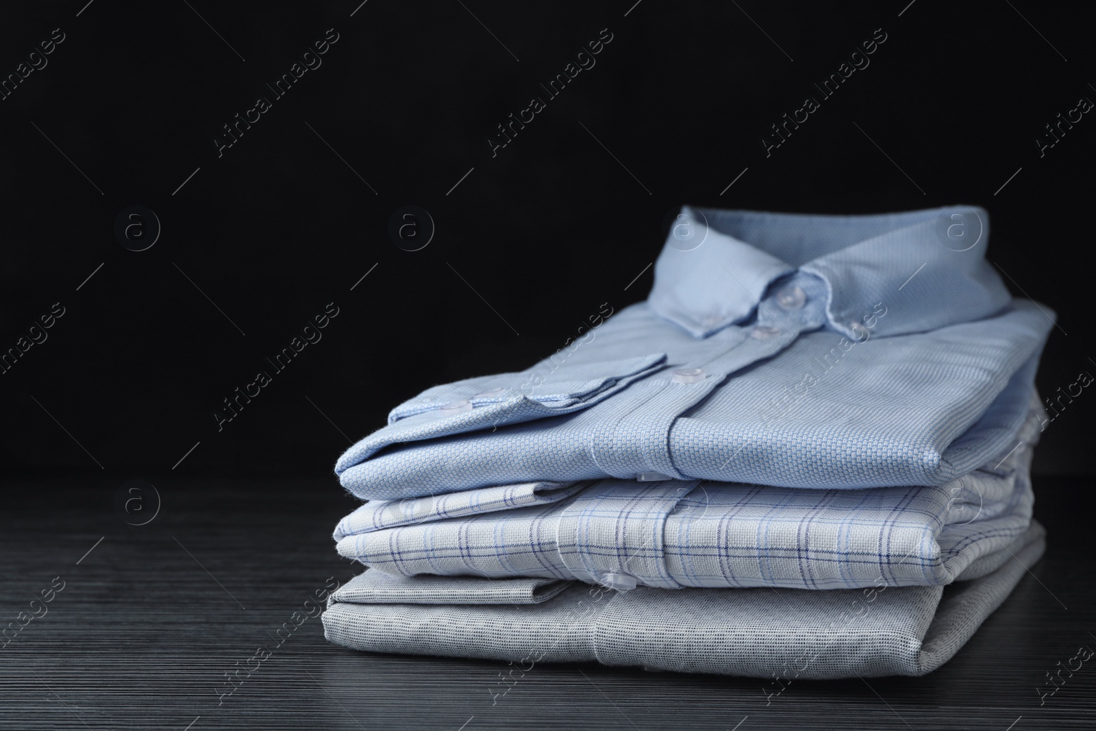 Photo of Stack of classic shirts on black wooden table