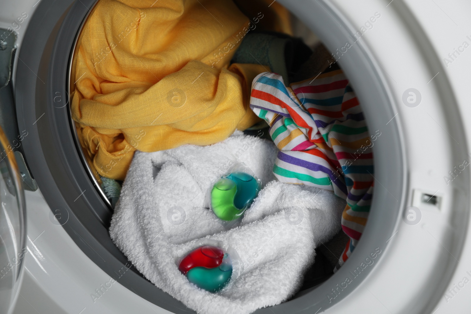 Photo of Laundry detergent capsules and clothes in washing machine drum, closeup view