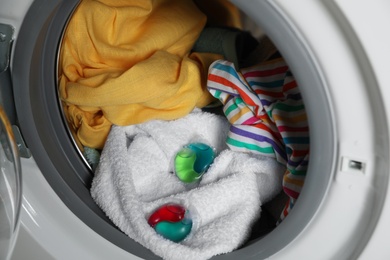 Photo of Laundry detergent capsules and clothes in washing machine drum, closeup view