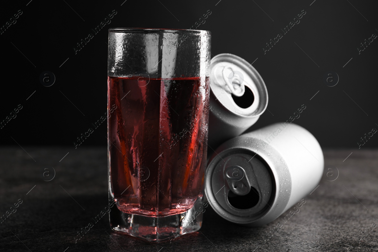 Photo of Energy drink in glass and aluminium cans on grey table, closeup