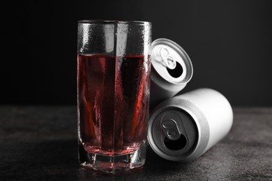 Photo of Energy drink in glass and aluminium cans on grey table, closeup