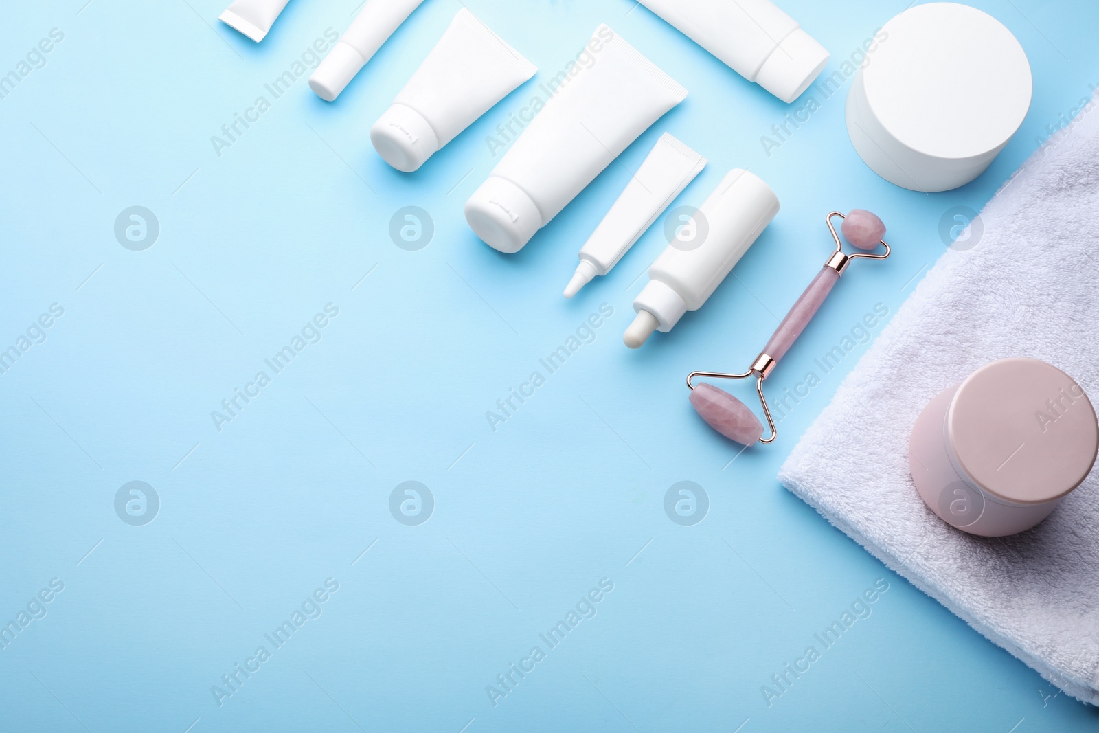 Photo of Natural face roller, cosmetic products and towel on light blue background, above view. Space for text