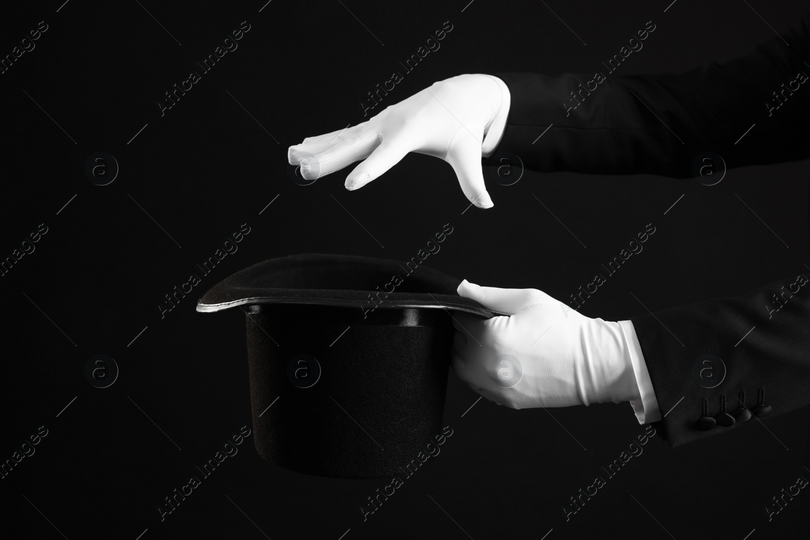 Photo of Magician showing magic trick with top hat on black background, closeup