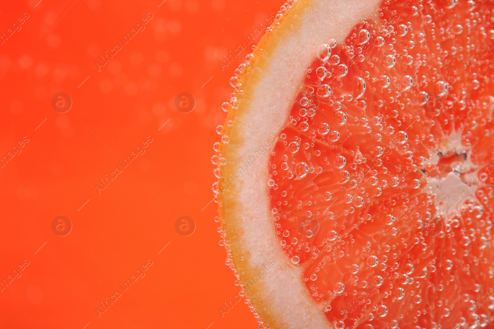 Photo of Slice of grapefruit in sparkling water on orange background, closeup with space for text. Citrus soda