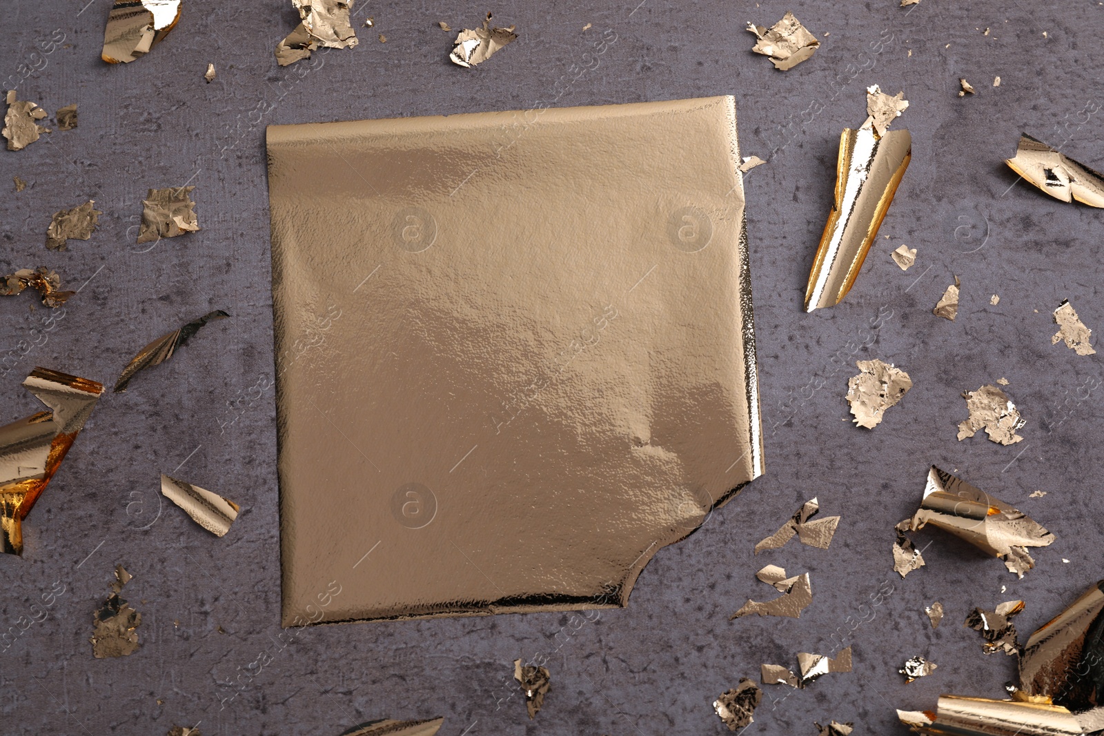 Photo of Edible gold leaf on grey textured table, flat lay