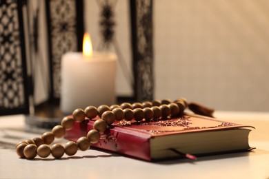 Photo of Arabic lantern, Quran and misbaha on white table, closeup