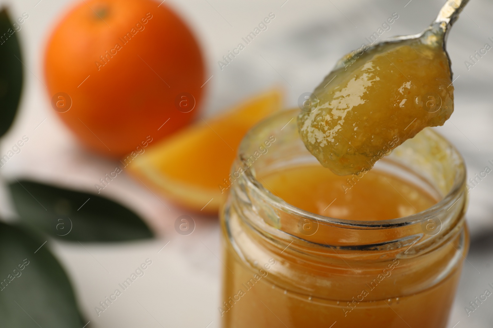 Photo of Spoon and jar with delicious orange marmalade on table, closeup. Space for text