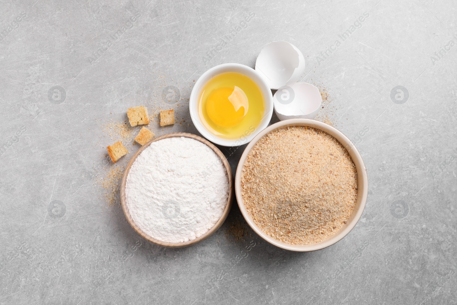 Photo of Fresh breadcrumbs, flour and egg on light grey table, flat lay