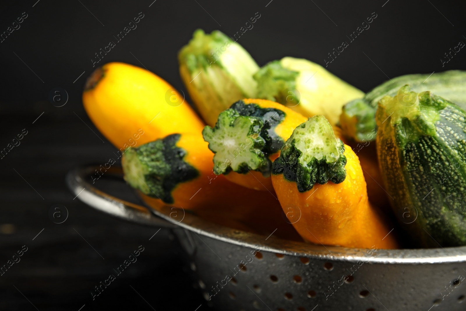 Photo of Colander with fresh ripe zucchini on dark background, closeup