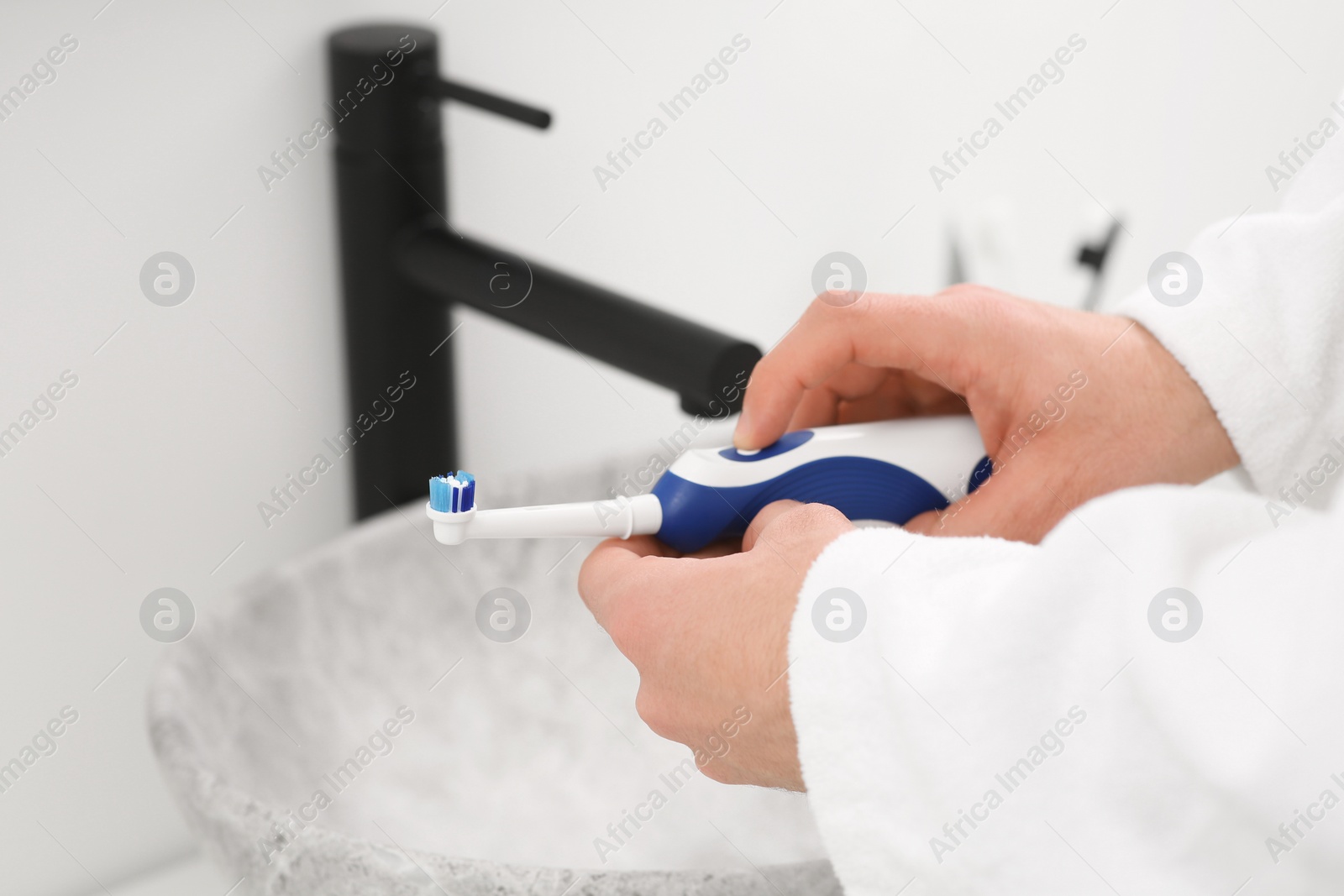 Photo of Man holding electric toothbrush near sink indoors, closeup