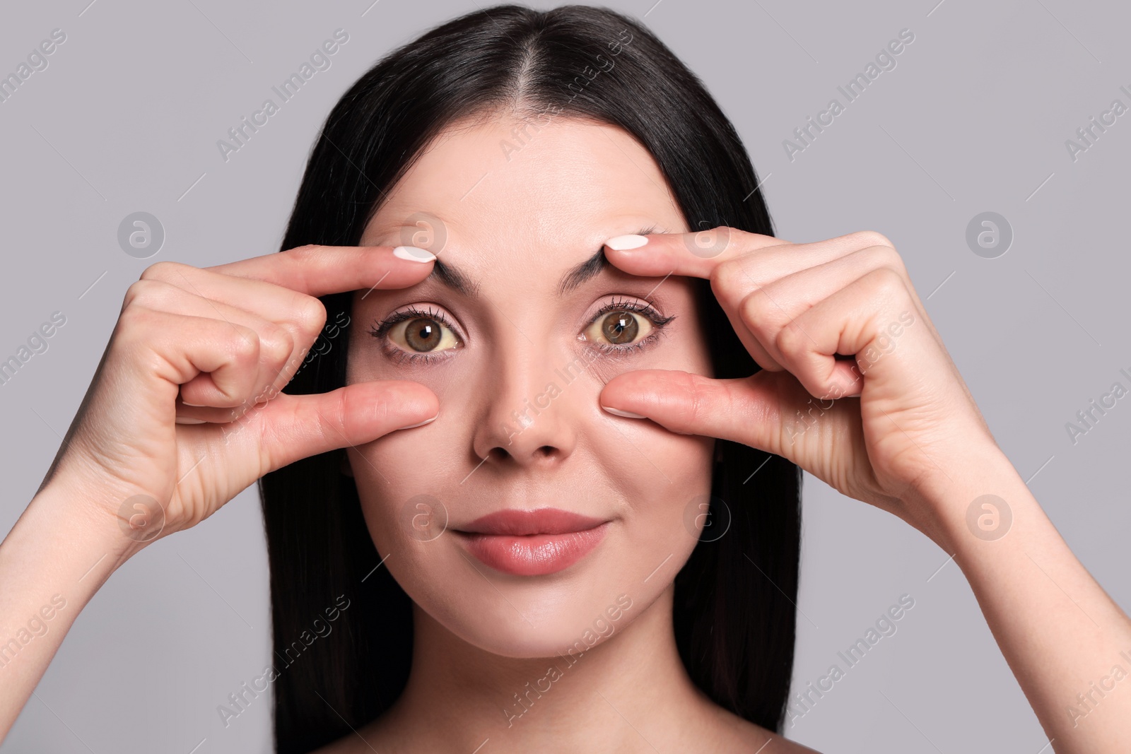 Photo of Woman checking her health condition on grey background. Yellow eyes as symptom of problems with liver