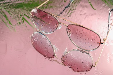 Photo of Stylish sunglasses with water drops on glass table, closeup