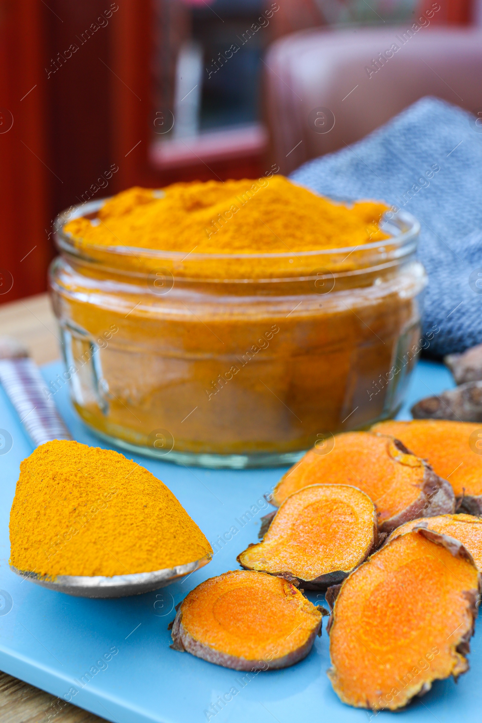 Photo of Glass jar of turmeric powder and roots on light blue tray, closeup