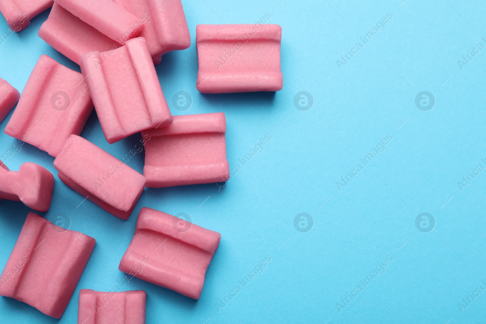 Photo of Tasty pink chewing gums on light blue background, flat lay. Space for text