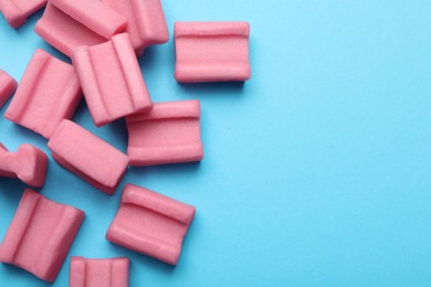 Photo of Tasty pink chewing gums on light blue background, flat lay. Space for text