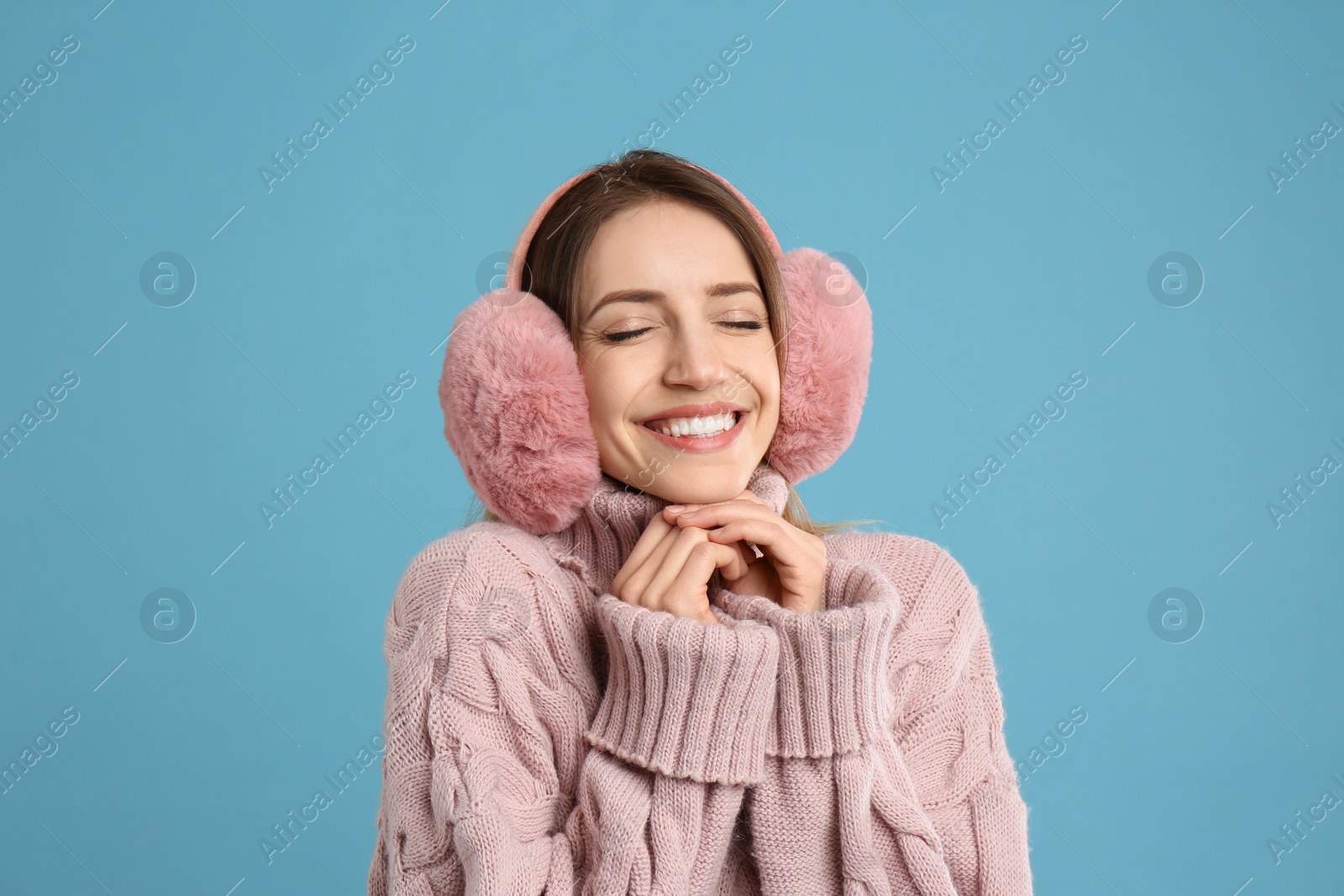 Photo of Happy woman wearing warm earmuffs on light blue background