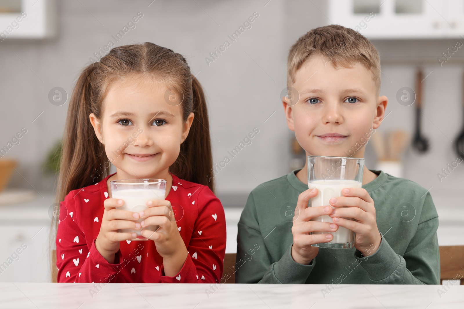 Photo of Cute children with glasses of milk at white table in kitchen