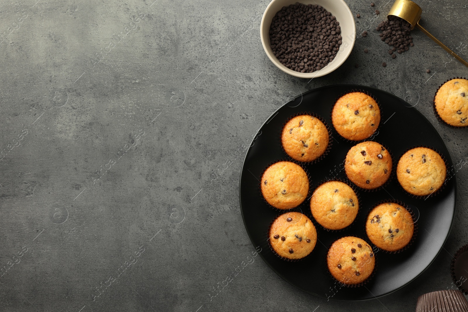 Photo of Delicious freshly baked muffins with chocolate chips on gray table, flat lay. Space for text