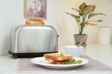Modern toaster with slices of bread on white table in kitchen