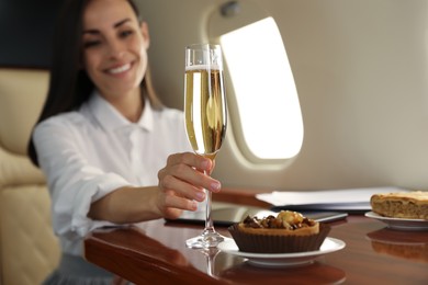 Photo of Woman with glass of champagne at table in airplane during flight, focus on hand