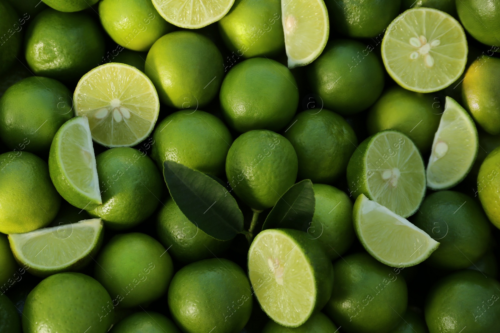 Photo of Whole and cut fresh ripe green limes as background, closeup view