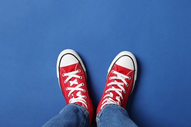 Photo of Woman in stylish gumshoes on blue background, top view