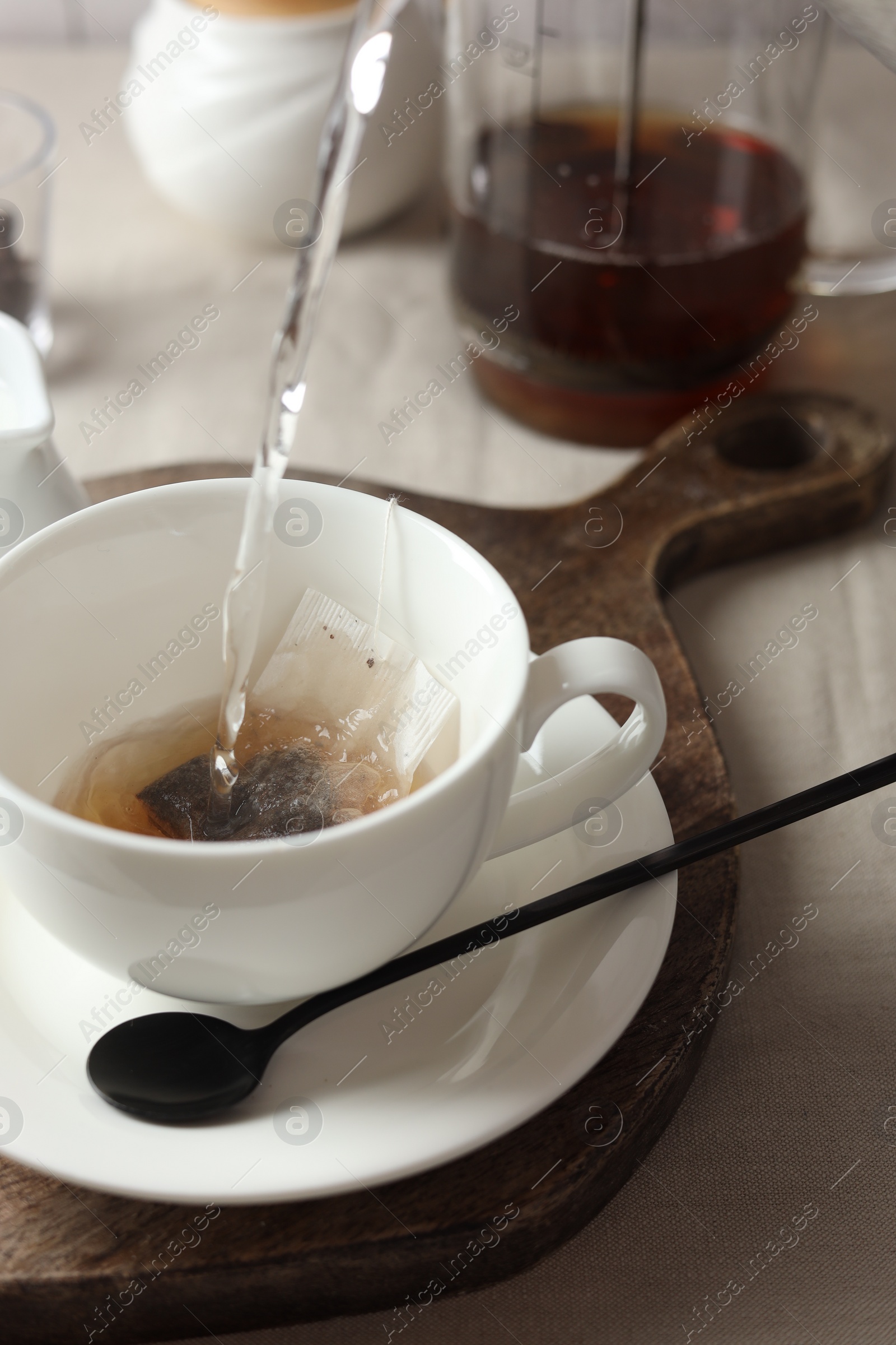 Photo of Pouring hot water into cup with tea bag on light table, closeup