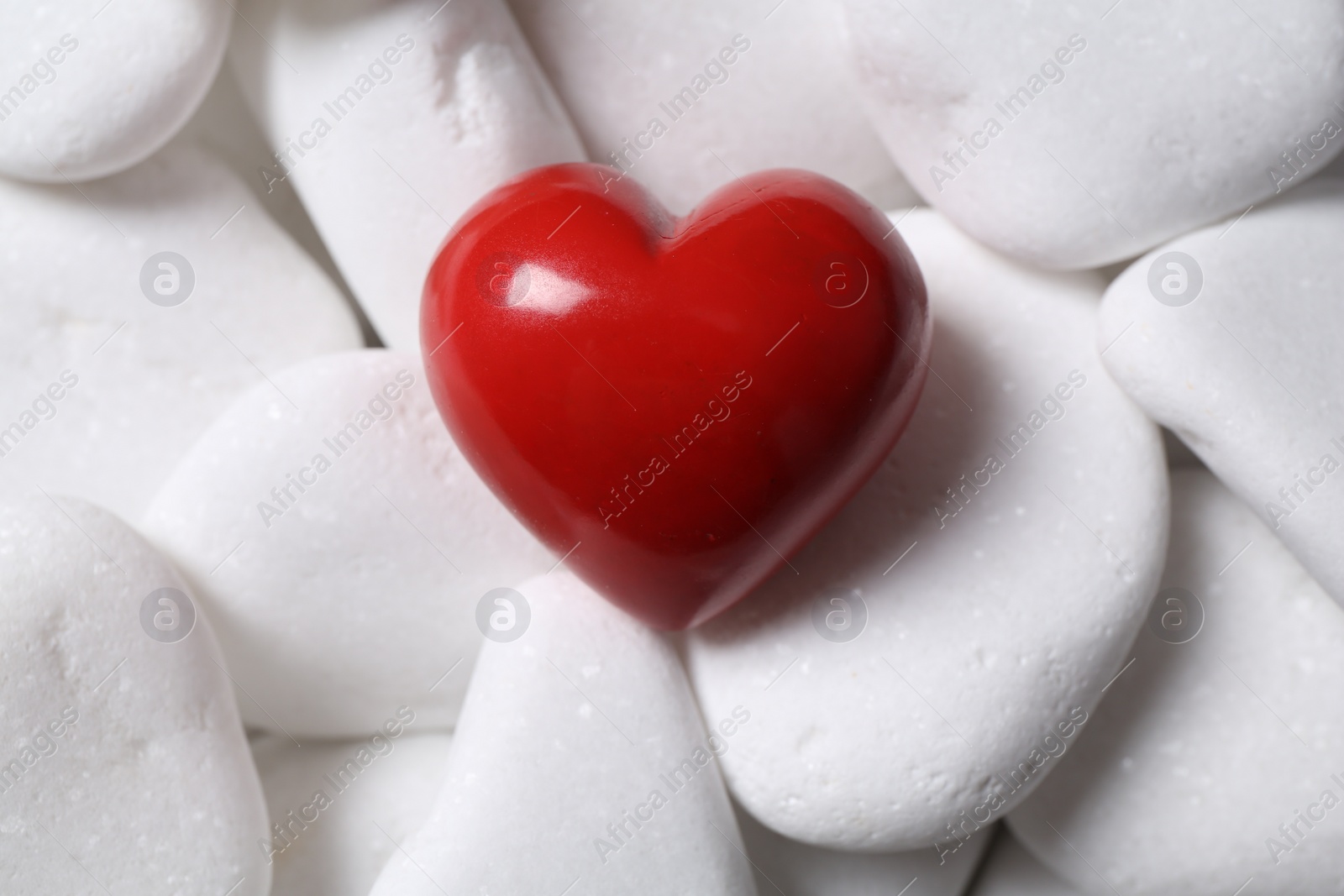 Photo of Decorative heart on white pebble stones, top view