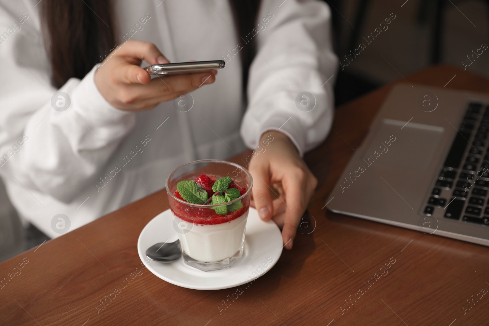 Photo of Young blogger taking picture of dessert at table in cafe, closeup