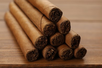 Photo of Many cigars on wooden table, closeup. Tobacco smoking