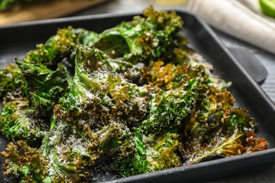 Photo of Tasty baked kale chips with cheese on table, closeup