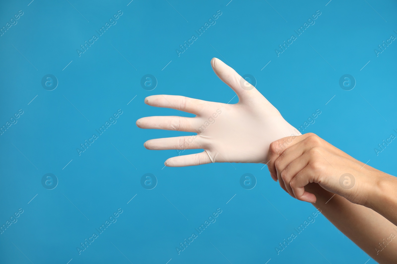 Photo of Doctor wearing medical gloves on light blue background, closeup