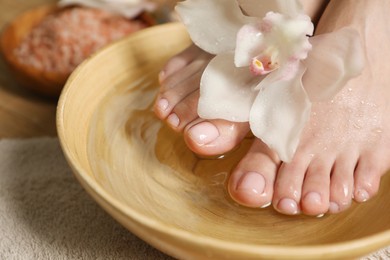 Photo of Woman soaking her feet in bowl with water and flower, closeup. Pedicure procedure